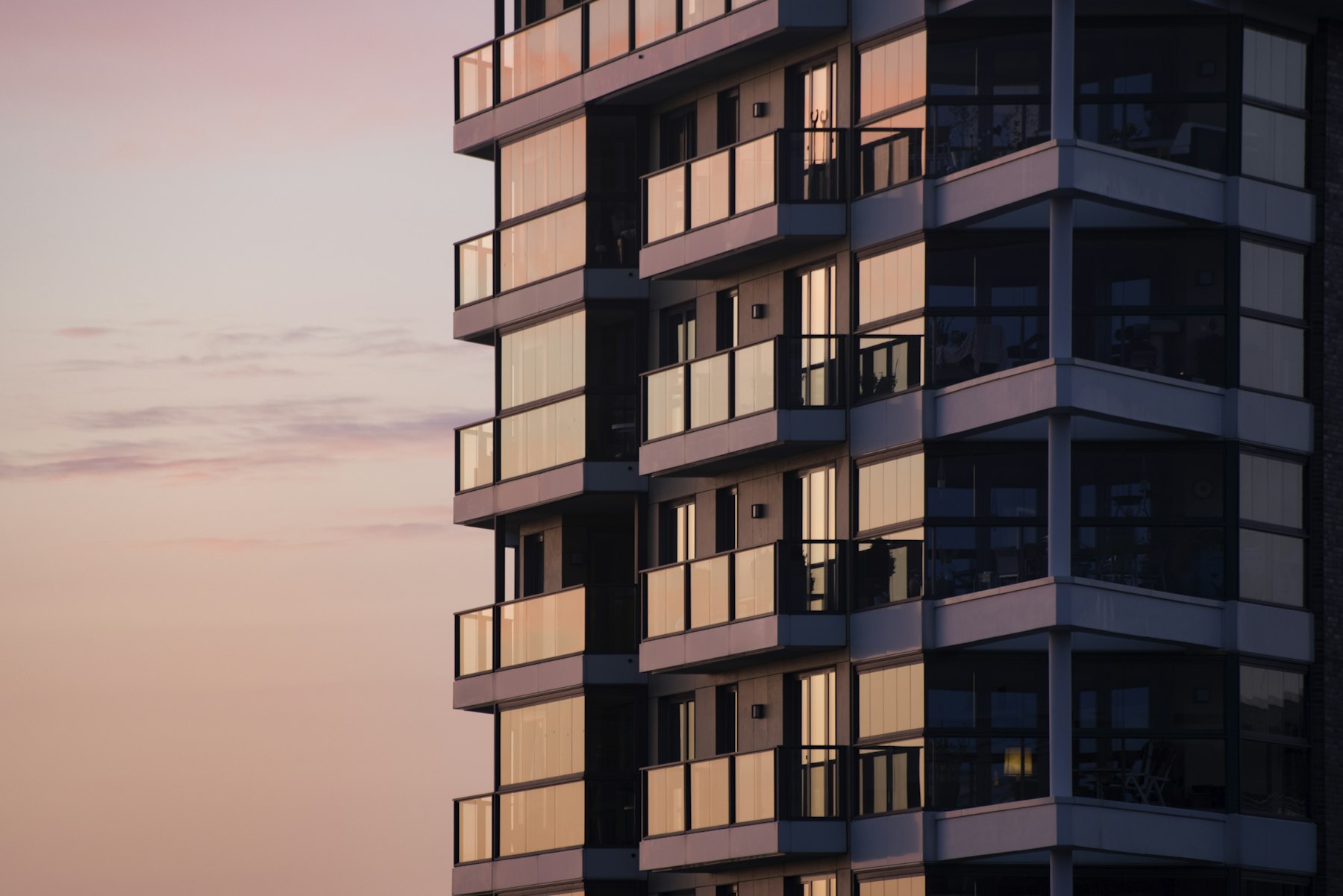 Fachada de un edificio residencial con balcones vidriados, al atardecer.